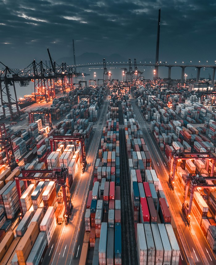 Seaport with stacked containers and cranes at dusk